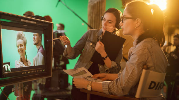 famous talented female director in chair looks at display spricht mit assistant, shooting blockbuster. green screen szene in historischen drama. film studio set professional crew doing high budget movie - filmregisseur stock-fotos und bilder