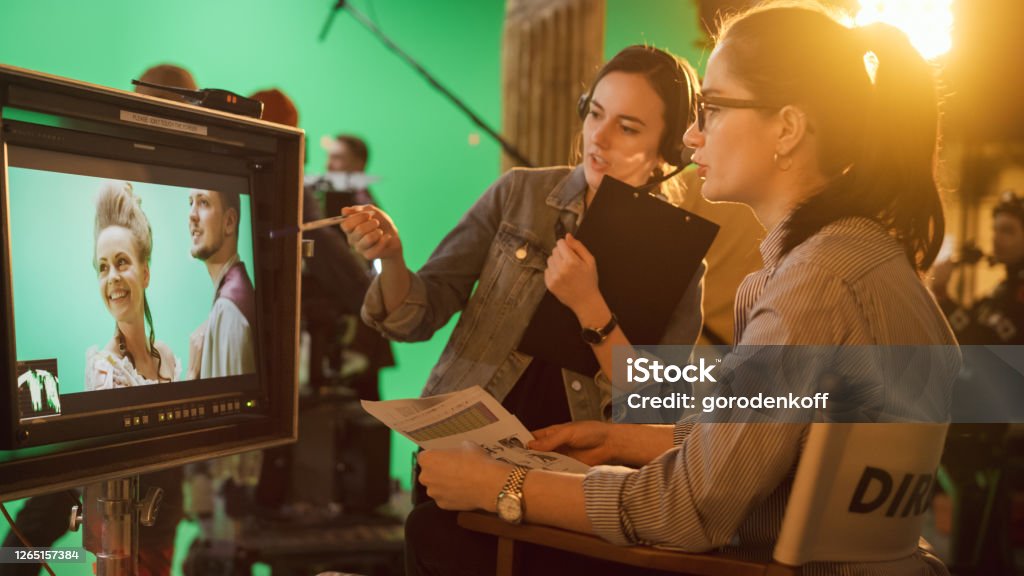 Famous Talented Female Director in Chair Looks at Display talks with Assistant, Shooting Blockbuster. Green Screen Scene in Historical Drama. Film Studio Set Professional Crew Doing High Budget Movie Movie Stock Photo