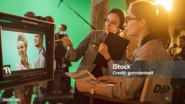 Famous Talented Female Director In Chair Looks At Display Talks With Assistant Shooting Blockbuster Green Screen Scene In Historical Drama Film Studio Set Professional Crew Doing High Budget Movie Stock Photo - Download Image Now