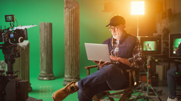 istock Prominent Successful Director Sitting in a Chair on a Break Using Laptop Computer. On the Studio Film Set with High-End Equipment Professional Crew Shooting High Budget Movie 1265157395