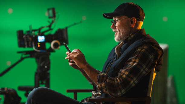 istock Prominent Successful Director Sitting in a Chair on a Break Using Smartphone. On the Studio Film Set with High-End Equipment Professional Crew Shooting High Budget Movie. 1265157410