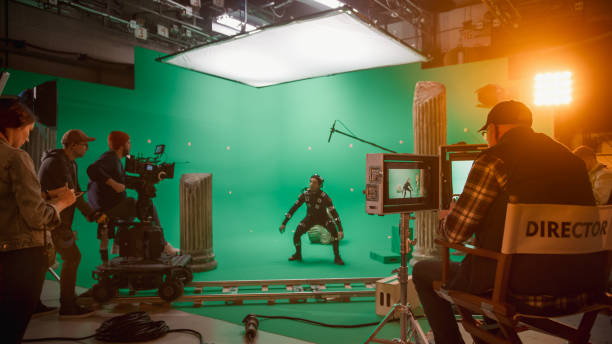 dans le big film studio professional crew shooting blockbuster movie. le réalisateur ordonne au caméraman de commencer à filmer la scène cgi de l’écran vert avec l’acteur portant un costume de capture de mouvement et une plate-forme de tête - acteur photos et images de collection