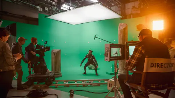 Photo of In the Big Film Studio Professional Crew Shooting Blockbuster Movie. Director Commands Cameraman to Start shooting Green Screen CGI Scene with Actor Wearing Motion Capture Suit and Head Rig