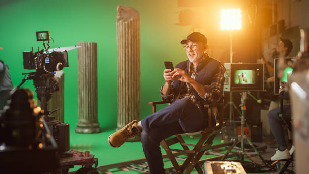 istock Prominent Successful Director Sitting in a Chair on a Break Using Smartphone. On the Studio Film Set with High-End Equipment Professional Crew Shooting High Budget Movie. 1265157453