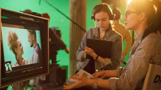 Photo of Famous Talented Female Director in Chair Looks at Display talks with Assistant, Shooting Blockbuster. Green Screen Scene in Historical Drama. Film Studio Set Professional Crew Doing High Budget Movie