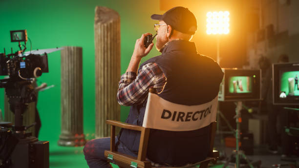 der prominente erfolgreiche senior director sitzt an seinem stuhl und befiehlt "action!", um mit den dreharbeiten zu beginnen. auf dem studiofilmset mit high-end-ausrüstung professionelle crew, die high-budget-film dreht - filmregisseur stock-fotos und bilder