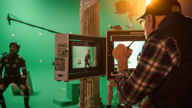 Director Looks at Displays Directs Green Screen CGI Scene with Actor Wearing Motion Tracking Suit and Head Rig. In the Big Film Studio Professional Crew Shooting Blockbuster Movie