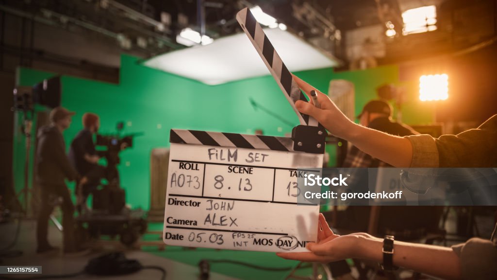 On Film Studio Set Camera Assistant Holds Clapperboard. Green Screen Scene with Talented Cameraman in the Background. Close-up Shot. Film Slate Stock Photo