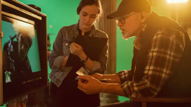 Photo of Director Looks at Display and Compares to Storyboard while Shooting Blockbuster Movie. Green Screen Scene with Actor Wearing Motion Caption Suit. Studio Set Professional Crew Doing High Budget Movie