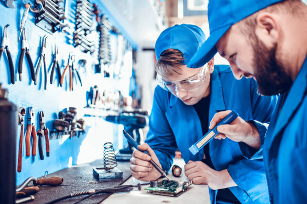 mechanic helping apprentice learn wire soldering and using light to see - men baseball cap focus determination imagens e fotografias de stock