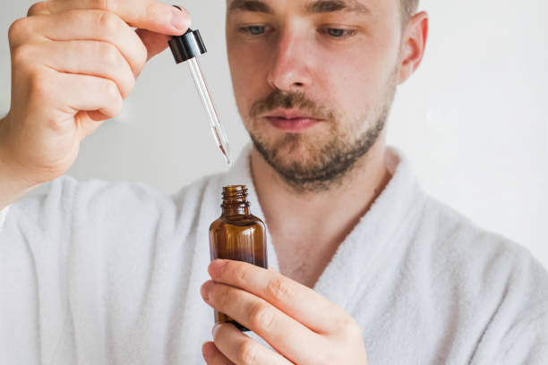 Young handsome man going to apply skin care product on his face. Close up of young handsome man in bathrobe going to apply serum or other skin care product on his face. Focus on the bottle blood serum photos stock pictures, royalty-free photos & images