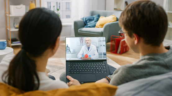 Young Couple of a Girl and Man Sitting at Home, Using Laptop Computer to Talk to a Doctor via Video Conference Medical App. They Have Conversation with Physician Using Online Video Chat Application.