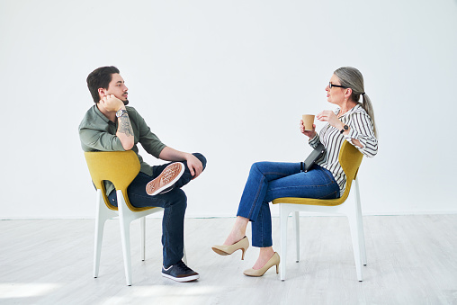 Shot of two businesspeople having a discussion while sitting on chairs in an office