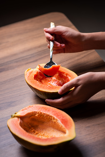 Female eating papaya fruit with a spoon on a wooden table top view