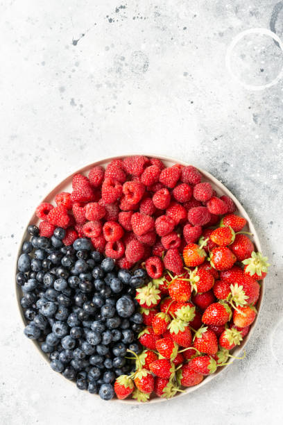 istock Fresh berries. Different berries in a white ceramic plate on a light table. Strawberries, raspberries and blueberries on a plate. Top view with space for text 1265173026