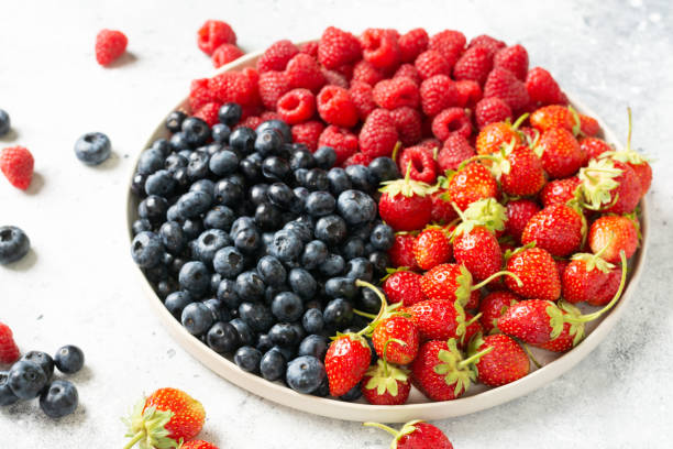 istock Fresh berries. Different berries in a white ceramic plate on a light table. Strawberries, raspberries and blueberries on a plate. Berries close up 1265173036
