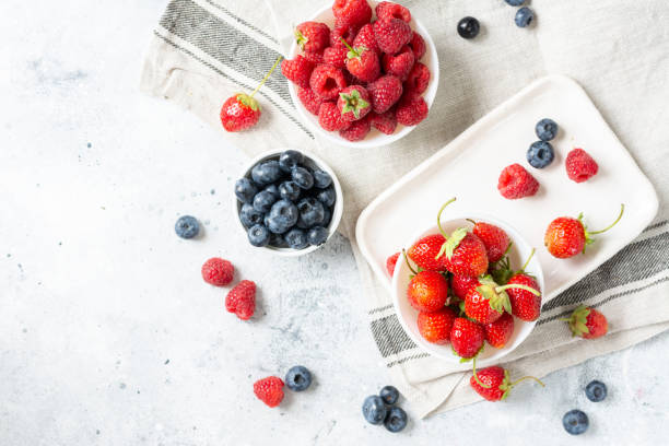 istock Ripe berries. Different berries in white ceramic bowls on a light table. Strawberries, raspberries and blueberries in plates against a white brick wall. Top view with space for text 1265173042
