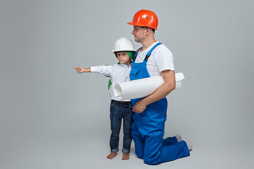 adult man with a young son in construction helmets. the child shows an imaginary house. the concept of the construction.