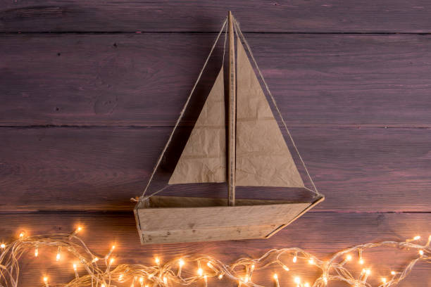 Travel and adventure creative concept - toy boat on a wooden background. Christmas lights as a sea waves stock photo