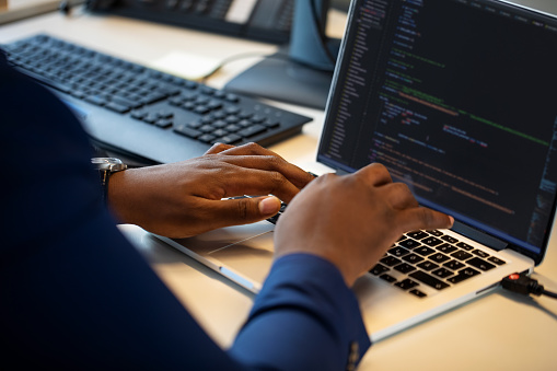 Close-up of businessman coding on laptop at his desk. Computer programmer working on laptop making new software program.