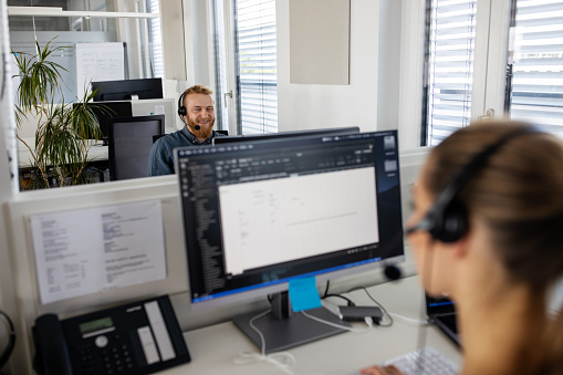 Smiling young man wearing headset working on computer in office. Customer service representative assisting clients in a call center.