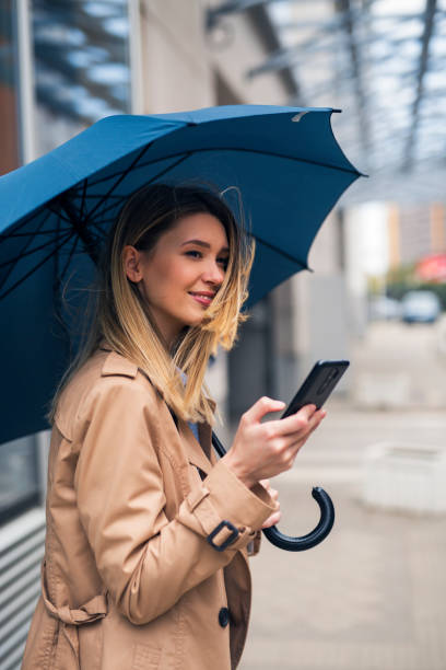 istock Smiling brunette holding smartphone and umbrella 1265178334