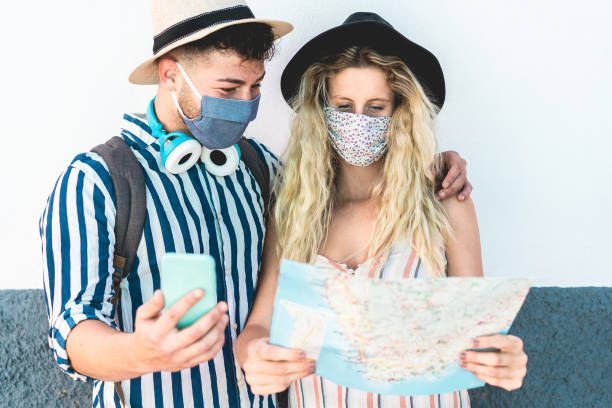 Young couple looking city map app during vacation tour while wearing face protective masks for coronavirus spread prevention - Travel, Covid 19 lifestyle and healthcare concept - Focus on girl face
