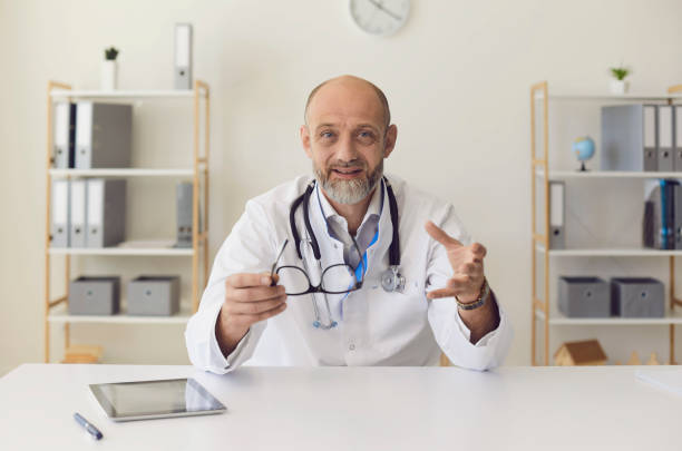 istock Senior experienced doctor speaks into camera with patient using gadget sitting in clinic office. Doctor online. 1265180966
