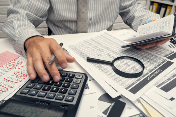 istock Business analysis and accounting concept - businessman working with document, spreadsheet, using calculator, tablet pc. Office desk closeup. 1265181072