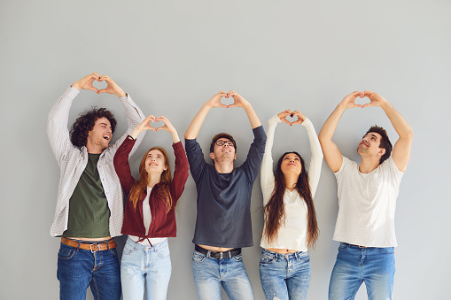 Group of friends making heart sign with hands on gray background. Friendship communication concept