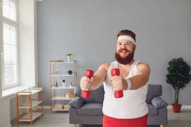 istock Funny fat man with dumbbells doing exercises in the room. 1265182420