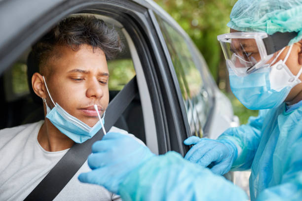 Concerned Man Getting COVID-19 Nasal Swab PCR Test at Drive-Thru Doctor taking coronavirus sample from male patient's nose. Healthcare workers are in protective workwear. They are standing by car during epidemic. pcr device photos stock pictures, royalty-free photos & images