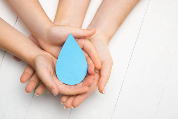 istock Human hands holding water drop isolated on white wooden background 1265185046