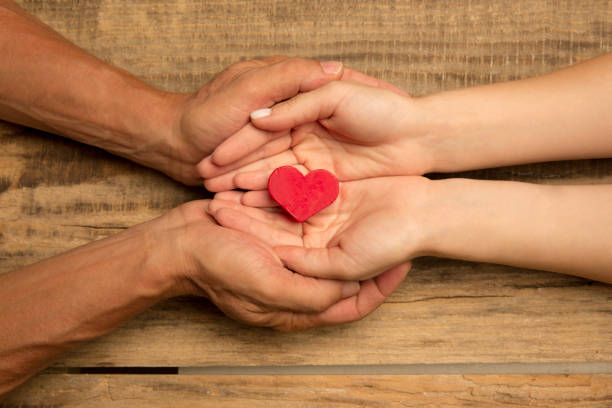 istock Human hands holding, giving heart isolated on wooden background 1265185111