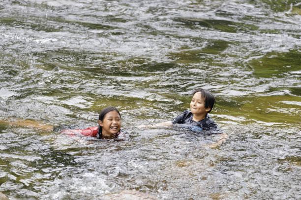 um par de meninos e meninas do ensino fundamental brincam no fluxo rápido na vila de kiriwong. - nakhon si thammarat - fotografias e filmes do acervo
