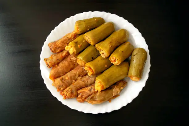 Photo of Traditional stuffed squash and cabbage rolls on white plate on dark wooden background