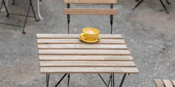 yellow empty cup for coffee on wooden surface of street cafe table outdoor