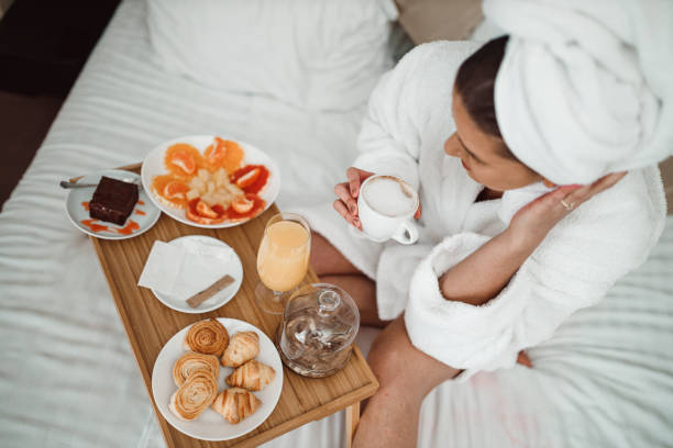 Woman drinking coffee and eating breakfast in bed Young woman wearing a bathrobe and a towel, sitting in a bed and drinking coffee and eating healthy breakfast from a wooden tray room service stock pictures, royalty-free photos & images