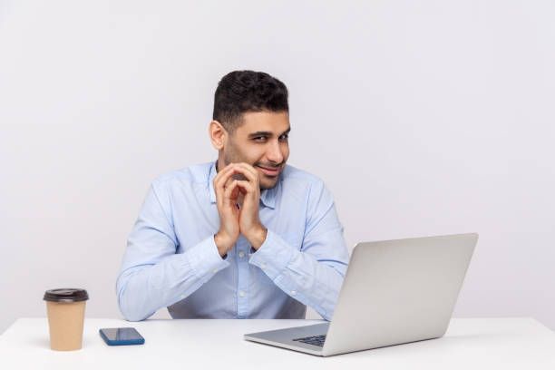 istock Sneaky scheming businessman sitting office workplace with laptop on desk, clasping hands and smirking 1265192133