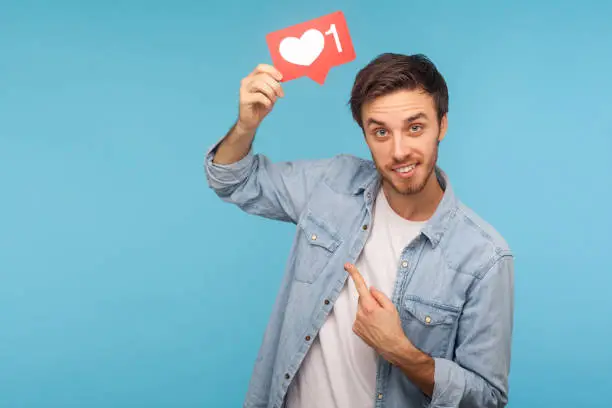 Photo of Click Like! Portrait of cheerful handsome blogger man in denim shirt pointing at social media heart Like button