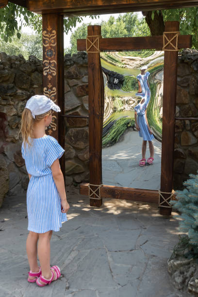 little girl in front of distorting mirror little girl in front of distorting mirror. funhouse mirror in a park distorted stock pictures, royalty-free photos & images