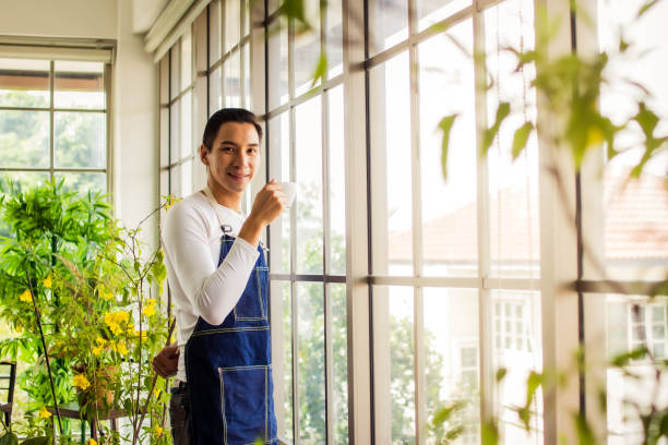 istock asia man holding cup coffee and standing near window coffee break time 1265192412