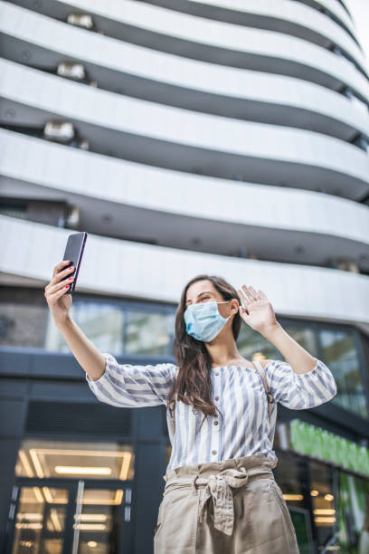 Young woman standing and using smart phone on city street with protective mask on her face. Virus pandemic and pollution concept. Young woman standing and using smart phone on city street with protective mask on her face. Virus pandemic and pollution concept. telephone voip dust internet stock pictures, royalty-free photos & images