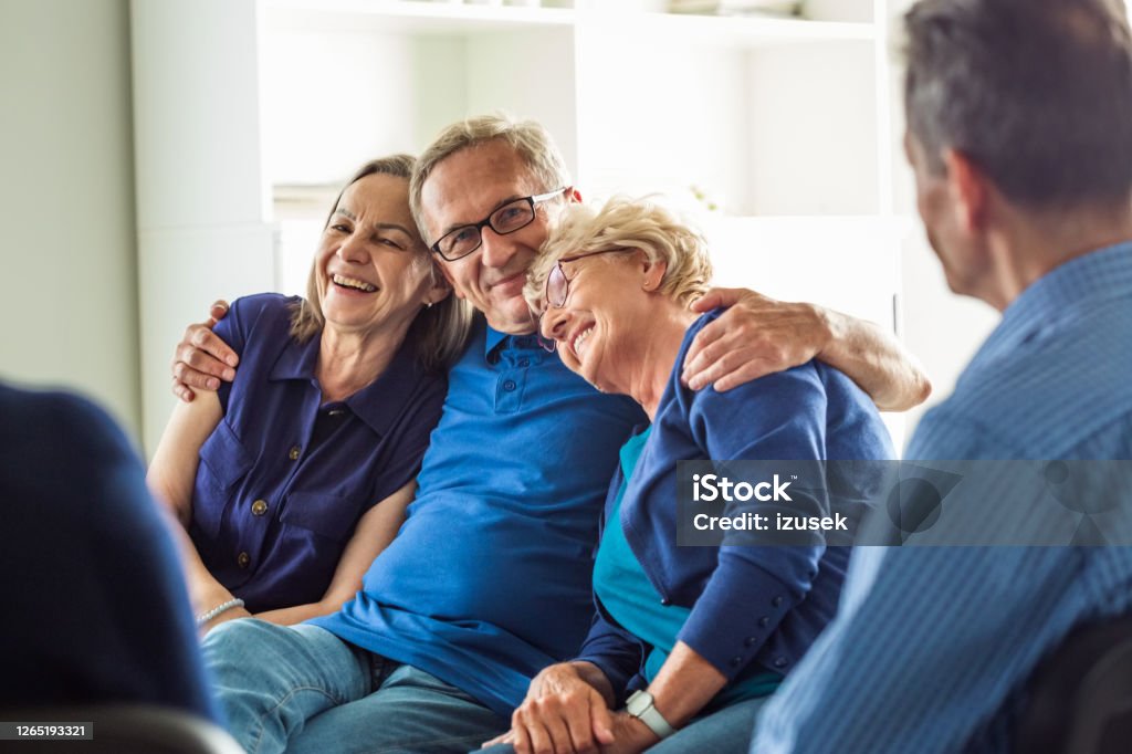 Cheerful senior people during group therapy Happy senior people sharing issues with patients during meeting in nursing home. Senior man embracing elderly ladies. Group Therapy Stock Photo