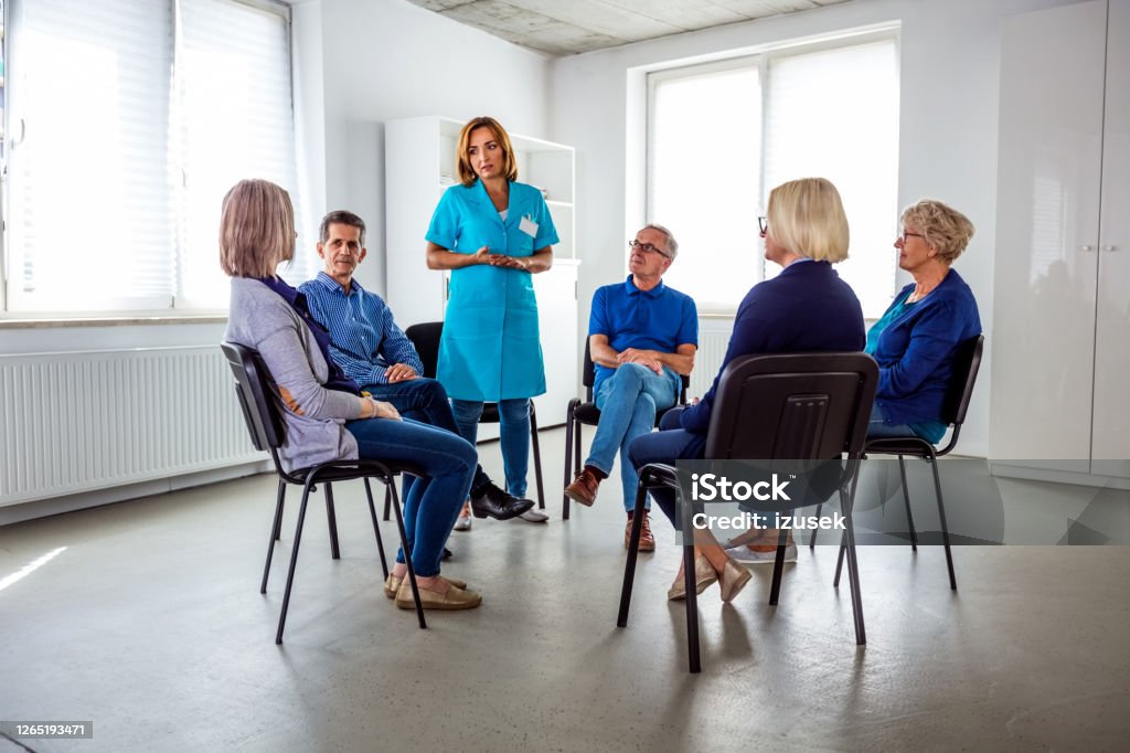 Nurse during meeting with senior people in nursing home Nurse taking with senior people during meeting in nursing home. They are discussing about mental wellbeing. Community Outreach Stock Photo