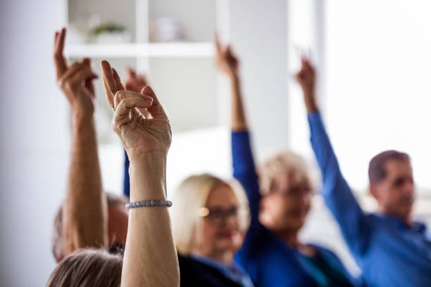 People voting during meeting in nursing home Senior people voting during group therapy, raising hands. They are discussing about mental wellbeing. Close up of hands. democracy stock pictures, royalty-free photos & images