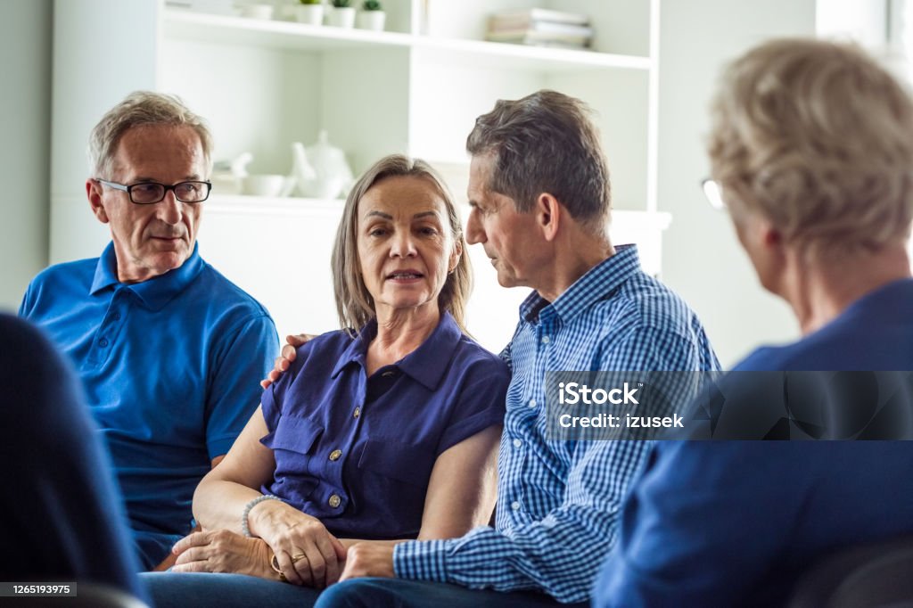 Senior couple sharing issues during meeting Senior people sharing issues with patients during meeting in nursing home. They are discussing about mental wellbeing. Embracing Stock Photo
