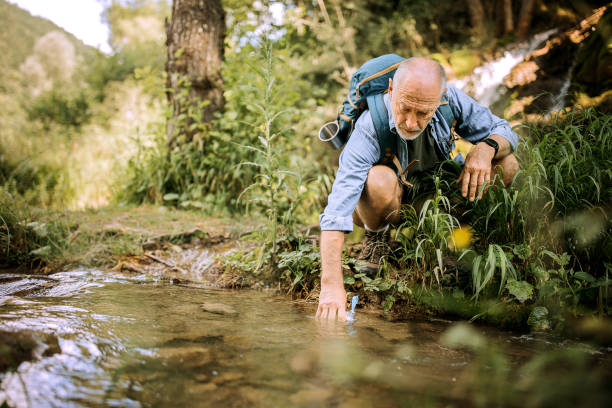istock Senior hiker refiling his water bottle in a small river 1265195080