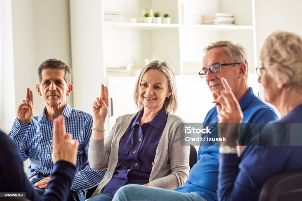 Senior people during group therapy Senior people sharing issues with patients and coach during meeting in nursing home. Mental health professional is sitting with people at community center. They are discussing about mental wellbeing, raising hands. 70-79 Years Stock Photo
