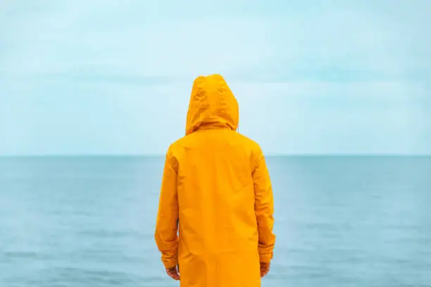 woman in yellow raincoat at sea beach cliff at storm rainy weather. summer vacation. travel concept. hiking